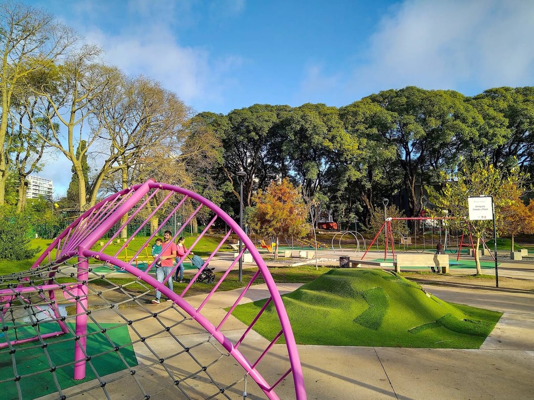 Juegos del espacio infantil Enriqueta Compte y Riqué en el Parque Rodó, con una familia paseando entre árboles altos