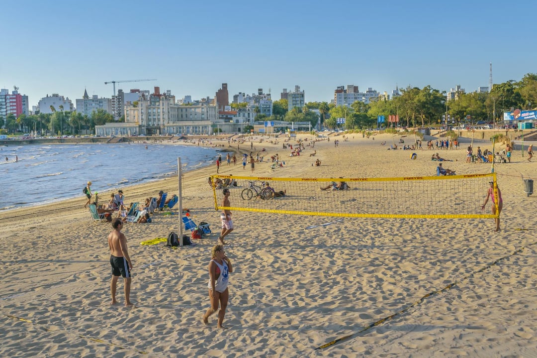 Gente jugando al vóley en la arena de la playa Ramírez, con el Parque Hotel y los edificios del barrio al fondo
