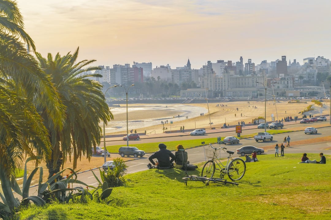 Playa Ramírez y la rambla al atardecer, con el Parque Hotel al fondo y gente sentada en el pasto