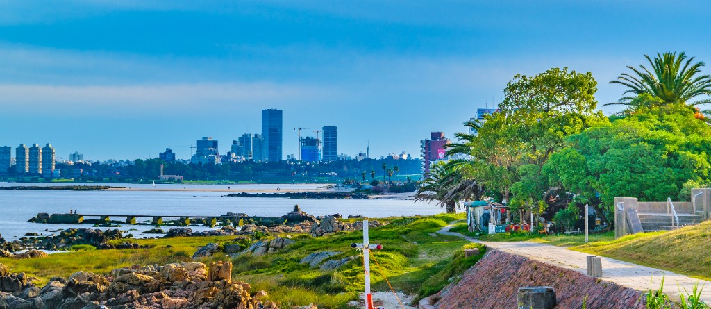 Rocas y césped de la rambla de Punta Gorda, con la playa y los edificios de la costa al fondo